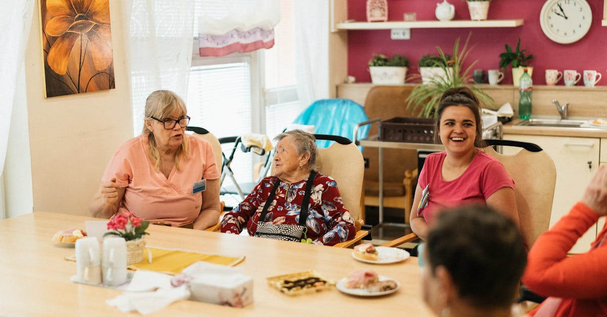 Elderly residents and caregivers enjoying a meal and conversation in a cheerful dining space.