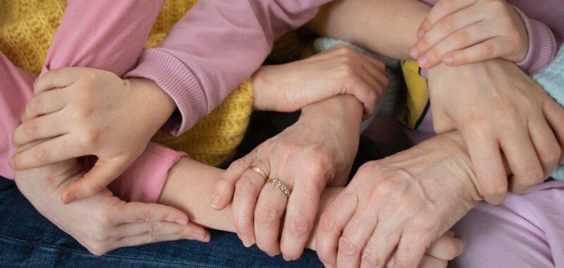 Multiple arms intertwined, symbolizing family unity and support across generations.